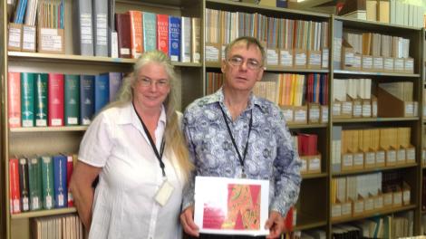 "Christine and Ian standing in front of a bookcase. He is holding his certificate of appreciation."